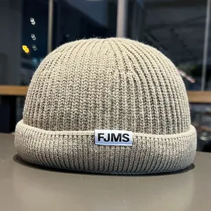 Close-up of the oatmeal grey ribbed knit texture and FJMS woven label on the miki hat