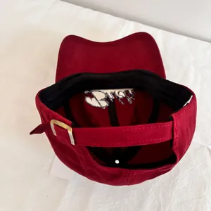 Detail view of burgundy baseball cap featuring a metal buckle and interior embroidery