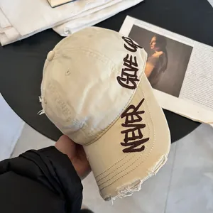 Detalle de gorra beige efecto desgastado con bordado Never Give Up y bordes deshilachados