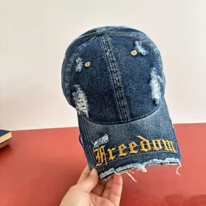 Dettaglio del ricamo gotico Freedom dorato su un cappellino in denim consumato