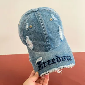 Dettaglio del cappellino in denim azzurro con ricamo Freedom e finitura con strappi
