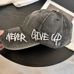 Detalle de gorra desgastada con bordado 3D NEVER GIVE UP y bordes deshilachados