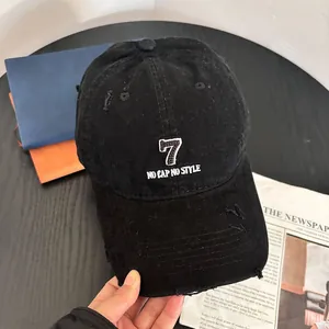 Detailed shot of black denim baseball cap with distressed holes and '7' embroidery
