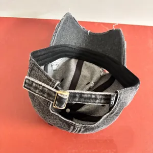 Dettaglio del berretto in denim grigio con cinturino regolabile e fibbia in bronzo