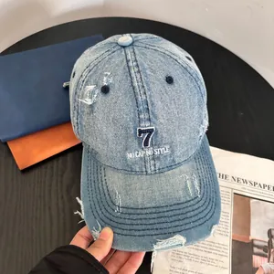 Detail of distressed light blue denim baseball cap with navy embroidery and ripped accents