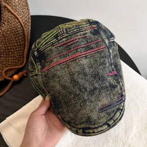 Detail of washed denim flat cap showing colorful embroidery stitching and fabric texture