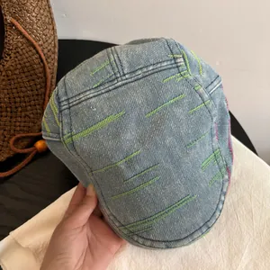 Detail of washed denim newsboy cap with decorative green and pink contrast stitching