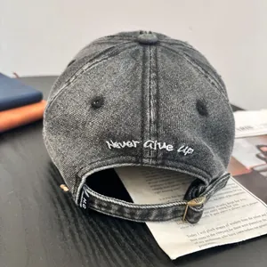 Macro shot of Never Give Up embroidery and metal buckle on washed denim baseball cap