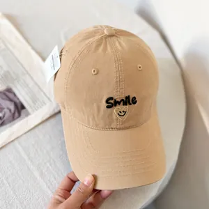 Detail of embroidered smile face and black lettering on a khaki cotton baseball cap