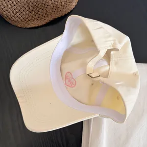 Detalle de gorra de algodón beige con bordado de corazón rosa interno y hebilla de metal