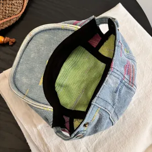 Detail view of denim beret featuring green striped lining and colorful stitching accents
