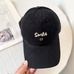 Detailed close-up of white Smile embroidery and smiley face on a black cotton baseball cap