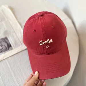 Detail of smile and letter embroidery on a deep red cotton baseball cap with curved brim