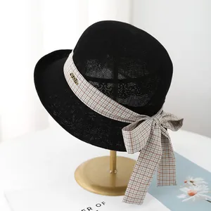 Women's black straw sun hat with plaid bow ribbon and elegant metal logo on a stand