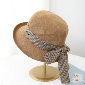 Detail of woven sun hat featuring a brown plaid ribbon bow and golden metal brand tag