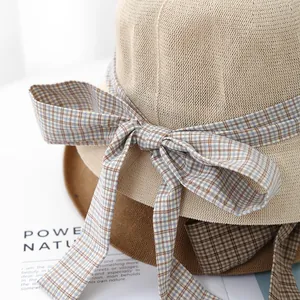 Detail of woven straw sun hats with elegant plaid ribbon bow in beige and brown