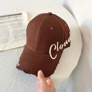 Detalle de gorra marrón oscuro con bordado Cloud blanco y borde de visera desgastado