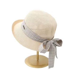 Women's cream straw sun hat with plaid ribbon bow and golden logo on a display stand