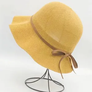 Detail of the yellow woven sun hat featuring a brown bow ribbon on a white background
