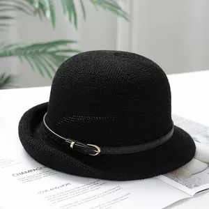 Detail of a black woven sun hat with a decorative leather belt buckle on a white table
