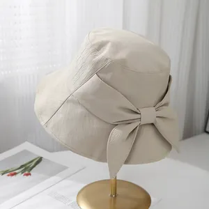 Chapeau de soleil beige à bord large avec un grand nœud élégant pour sorties d'été