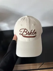 Detalle de una gorra de béisbol de lona beige con bordado cursivo Brkln en color marrón