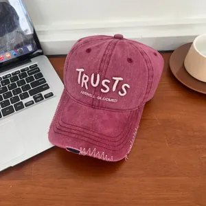 Macro detail of wine red distressed baseball cap with white TRUSTS letter embroidery