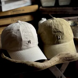 Minimalist washed canvas baseball caps with metal H logo in beige and olive green
