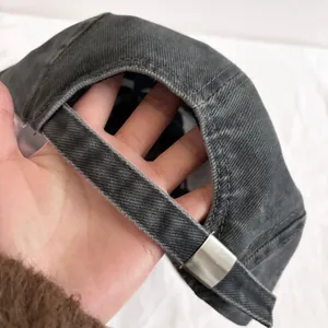 Detail of adjustable metal buckle and webbing on washed denim baseball cap