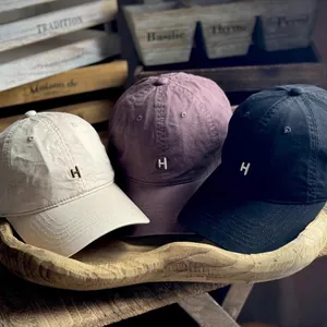 Three washed cotton baseball caps with embroidered H logo on a rustic wooden tray