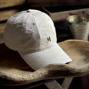 Close-up of letter H embroidery on a beige washed cotton baseball cap with stitched brim