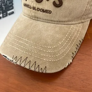 Detailed macro view of distressed khaki baseball cap with embroidered letters and contrast stitching