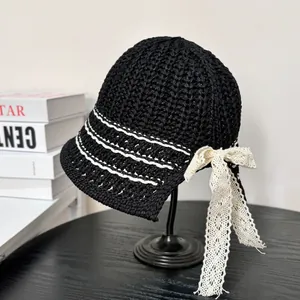 Detail of knitted black sun hat with white stripes and elegant beige lace bow decoration
