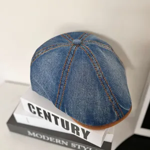 Retro denim beret with orange stitching and brown leather trim on white background