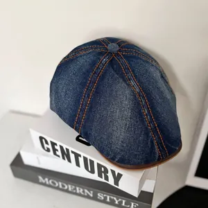 Detailed view of dark blue denim newsboy cap with orange stitching and leather trim
