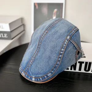 Detailansicht der blauen Denim-Baskenmütze mit braunen Kontrastnähten auf schwarzer Fläche