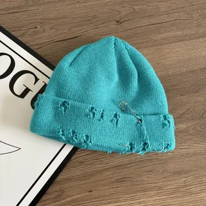 Dettaglio del berretto in maglia blu acceso con anelli d'argento, spilla e effetto usurato