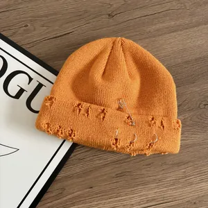 Dettaglio del berretto in maglia arancione con anelli di metallo e spille di sicurezza