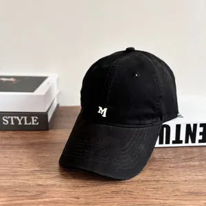 Detail of black cotton baseball cap featuring white embroidered letter M on the front