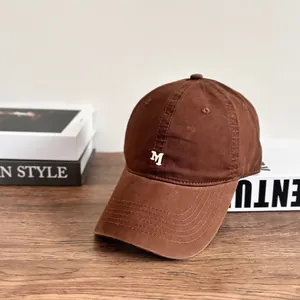 Brown cotton washed baseball cap with white 3D M embroidery on a wooden table
