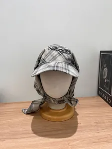Detail of grey plaid beret cap with integrated scarf ties and fine embroidery