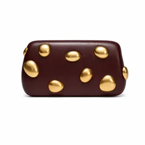 Detail view of burgundy leather clutch with irregular polished gold metal pebbles