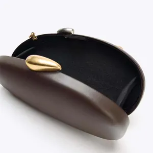 Detail of dark brown hard shell clutch bag with gold teardrop clasp and black interior