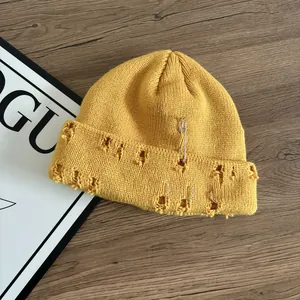 Dettaglio del berretto in maglia zenzero con spille e anelli su fondo in legno