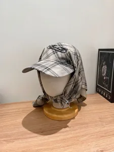 Close-up of grey plaid beret with integrated scarf and black embroidered logo detail