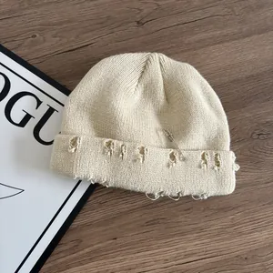 Dettaglio del berretto in maglia crema effetto vissuto con spilla da balia e anelli in metallo