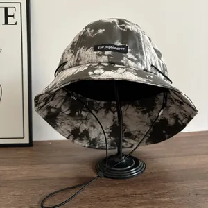 Dettaglio del cappello pescatore tie-dye con patch logo e cordino antivento regolabile