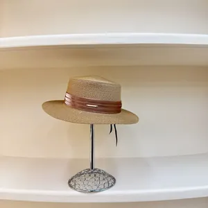 Detalle de la textura tejida y la cinta marrón con logo metálico en el sombrero