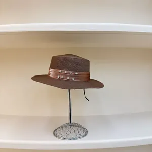 Detalle de sombrero de paja marrón con cinta de pedrería en un soporte de metal plateado