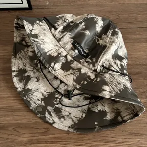 Dettaglio cappello a secchiello tie-dye con coulisse antivento ed etichetta del marchio